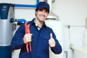 A plumber in coveralls with a water heater tank behind him